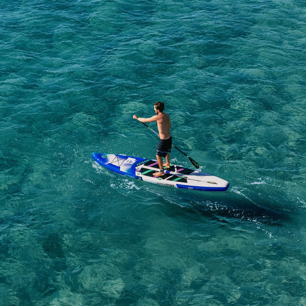 Persona remando en el SUP inflable Aztron Super Nova 11’0 en agua turquesa, vista aérea