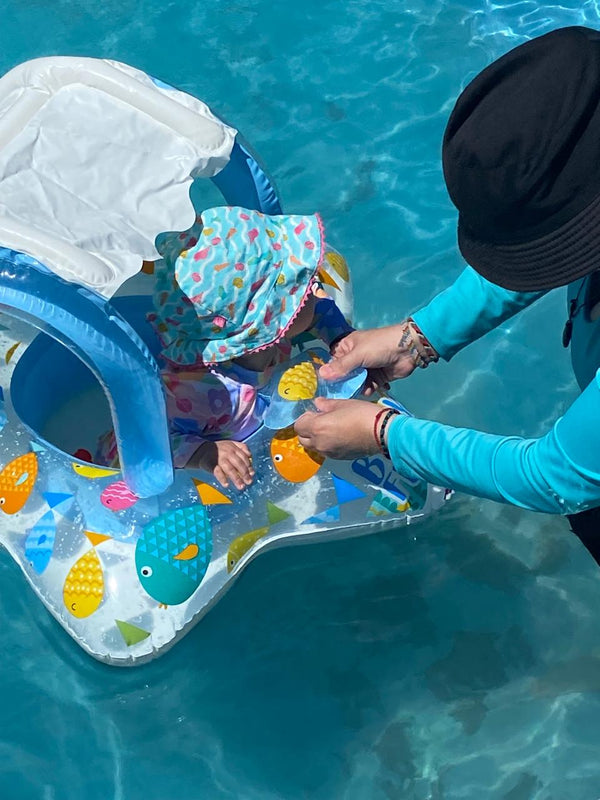 Bebé con gorro sentado en un flotador INTEX con asiento dentro de una piscina