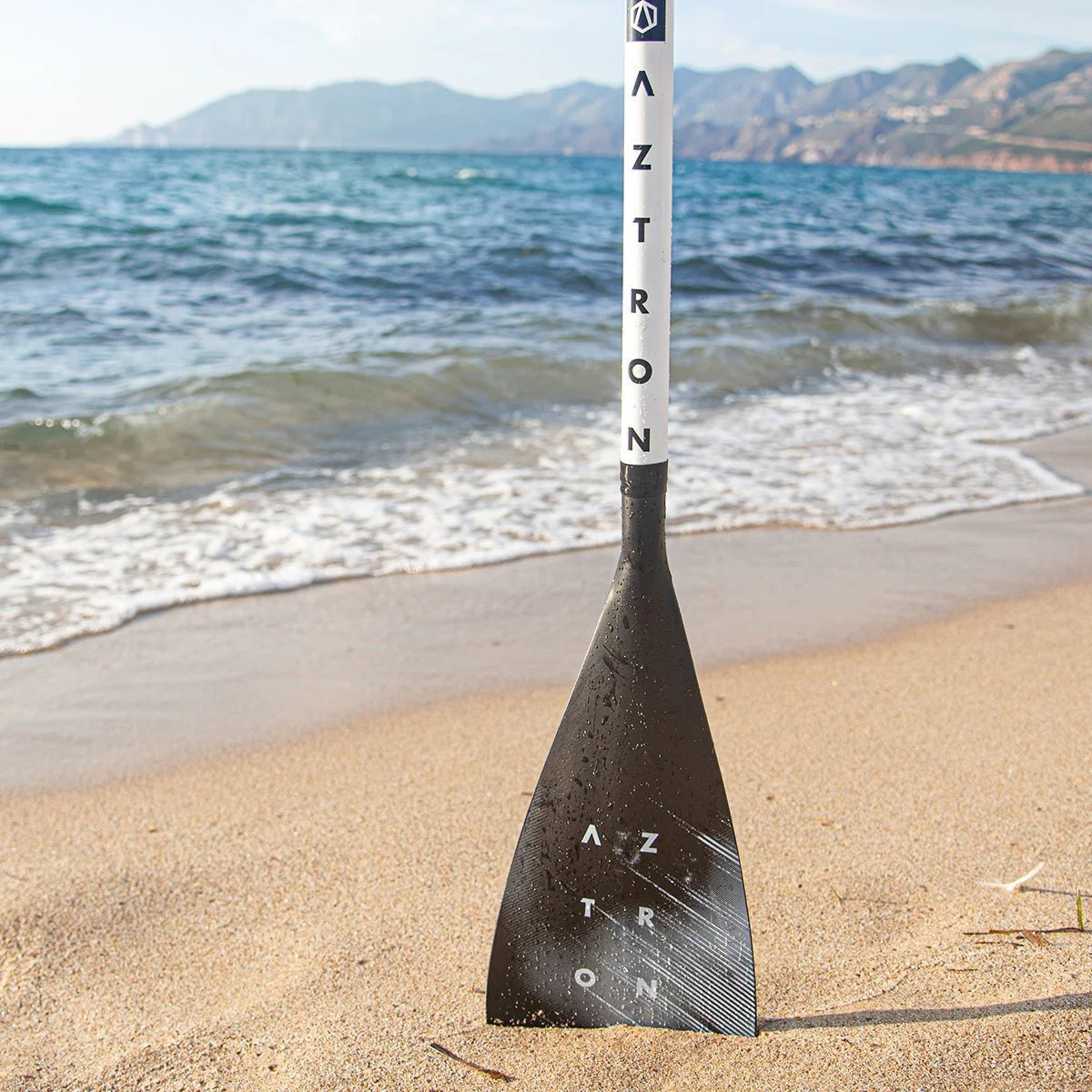 Remo de SUP Aztron Style de aluminio apoyado en la arena frente al mar