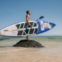 Hombre en la playa sosteniendo el SUP inflable Aztron Super Nova 11’0 y su remo