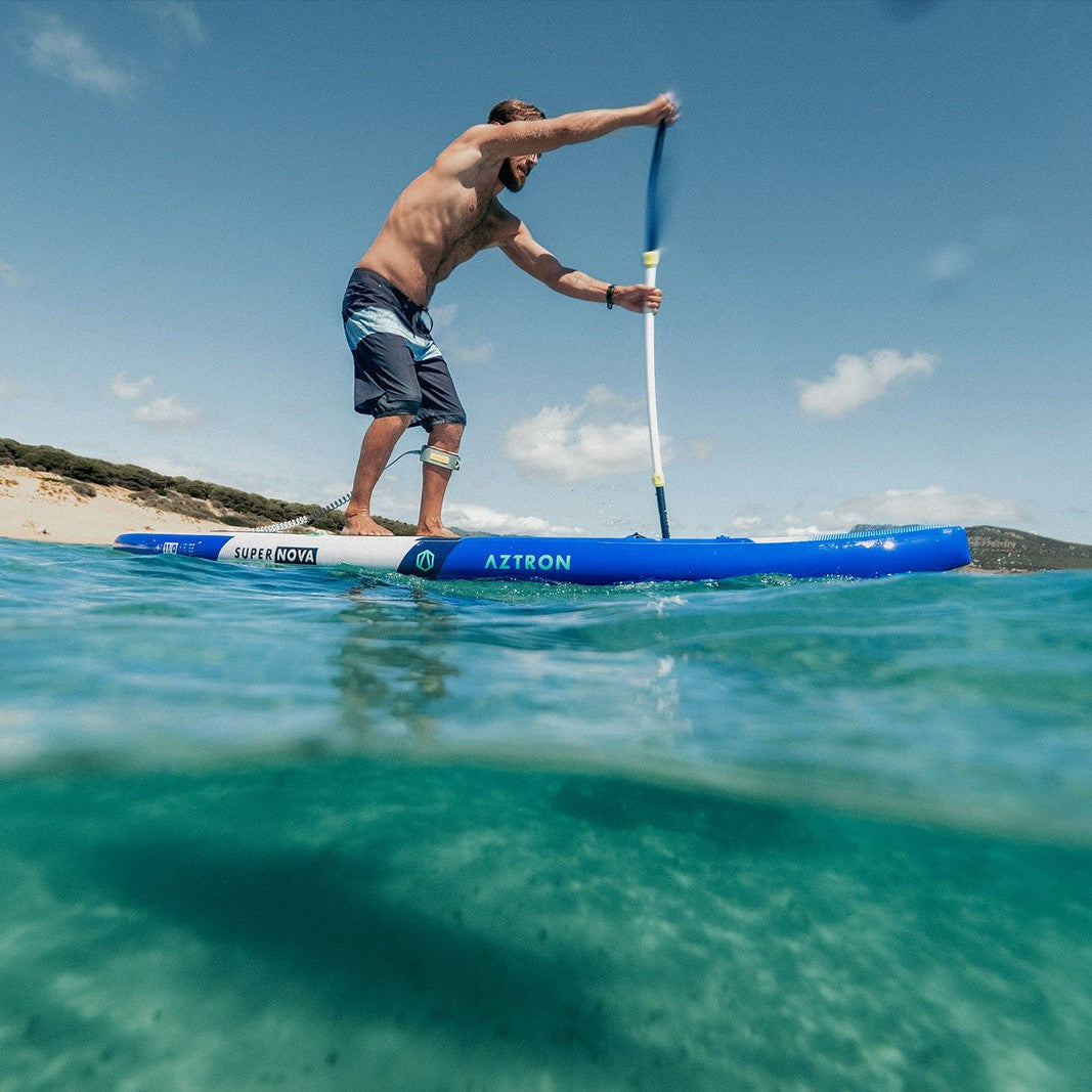 Hombre remando de pie en el SUP inflable Aztron Super Nova 11’0 cerca de la orilla