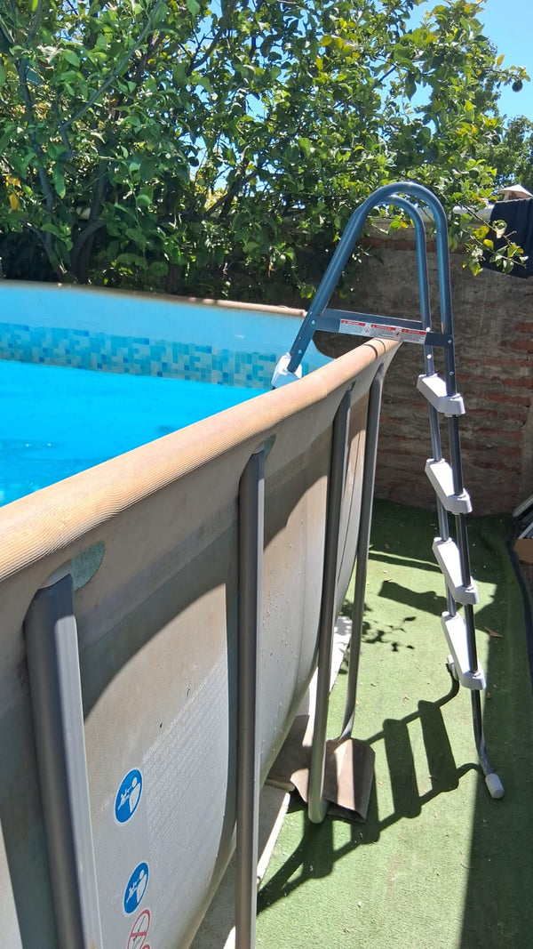 Escalera INTEX apoyada en el borde de una piscina estructural, vista desde el patio